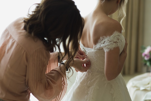 Bridesmaid is helping the bride to dress