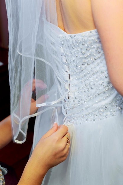 Bridesmaid tying bow on wedding dress mother helping bride dress