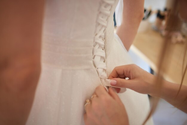 Bridesmaids dressing bride in the morning in hotel room girls helping bride put on stylish gown back view on ribbons and hands getting ready