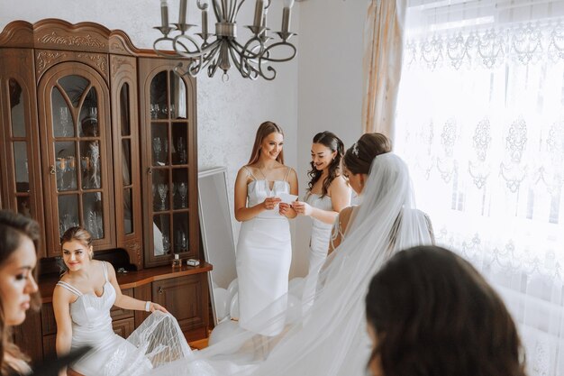 Le damigelle di sposa si rallegrano la mattina aiutando a fissare i bottoni del vestito da sposa e a prepararsi per la cerimonia nuziale prendono foto sorridono aiutano la sposa con le scarpe