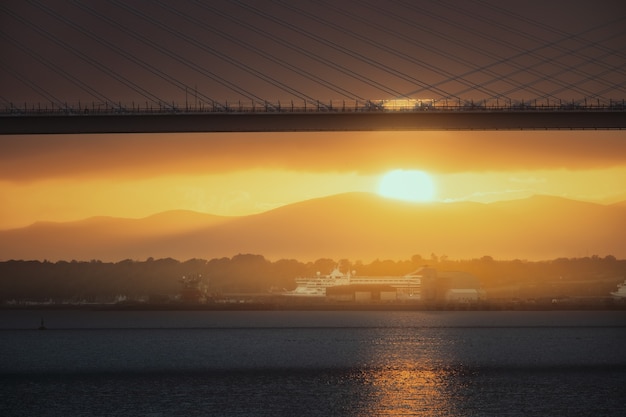 写真 夕日と海の向こうの道路橋とクイーンズフェリーがスコットランドを横断する船に橋を架ける...