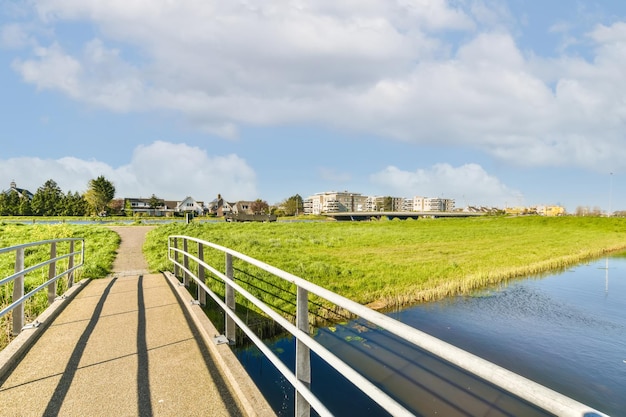 Photo a bridge over a body of water with buildings in the background and green grass on both sides under a blue sky