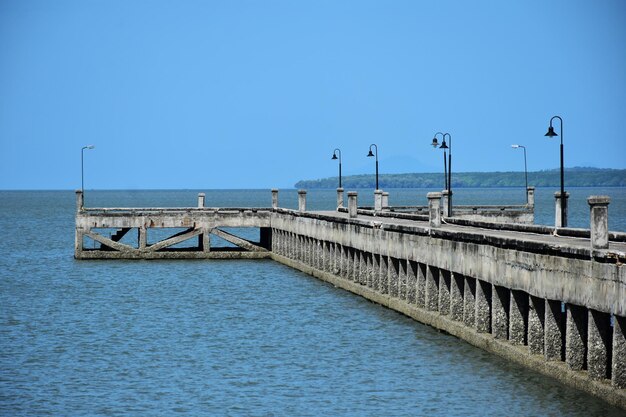 Bridge over calm blue sea against clear sky