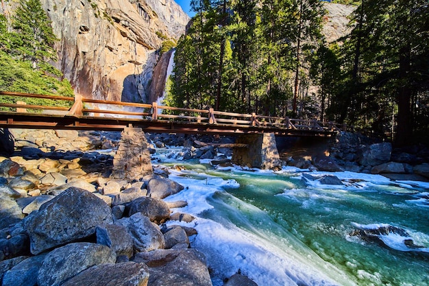 Мост через опасную слякотную холодную реку с нижним водопадом Йосемити на заднем плане и скалами