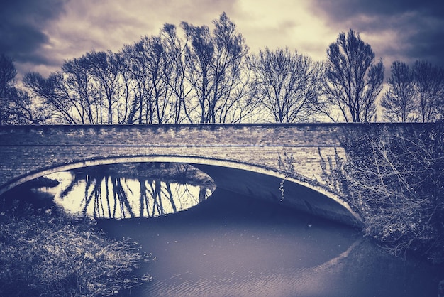 Bridge over river by bare trees against sky during sunset