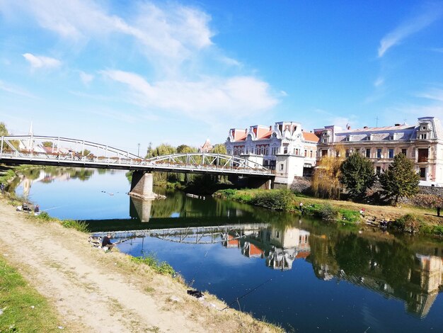 Bridge over river by buildings against blue sky