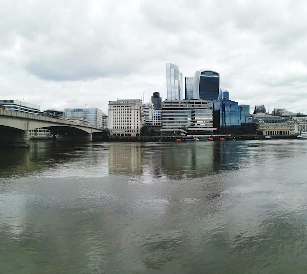 Photo bridge over river by buildings against sky