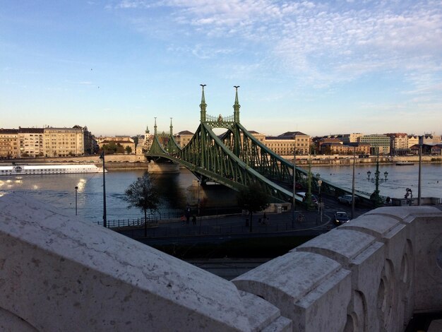 Bridge over river by buildings in city against sky