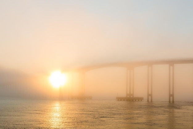 Bridge over river in foggy weather during sunset