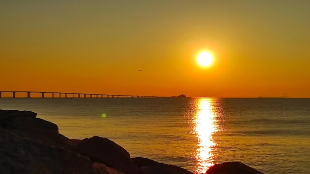 A bridge over the water with a sun setting behind it