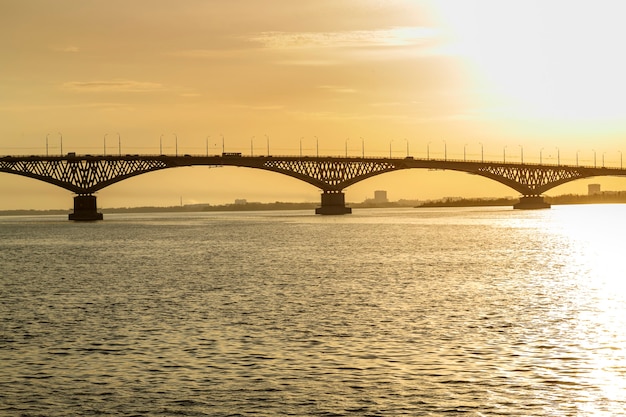 Foto ponte su un ampio fiume sotto i raggi del sole al tramonto.