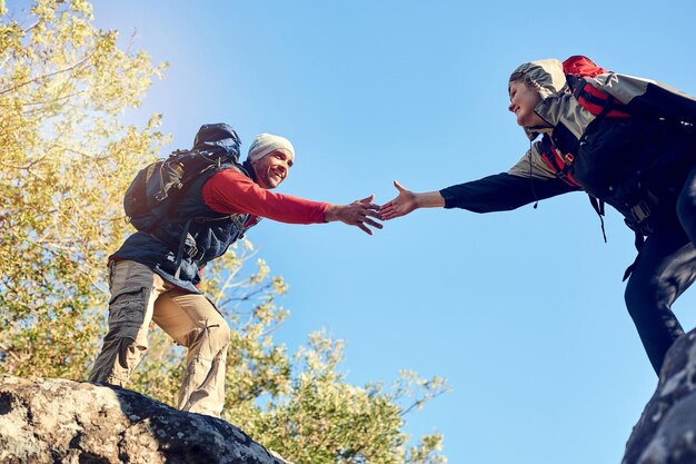 チームワークで分断を埋める幸せなハイカーのペアが登山道でお互いに手を伸ばすショット