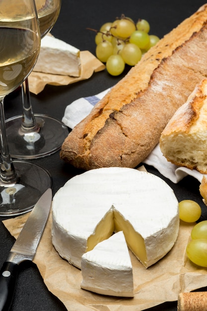 Сыр Бри, багет и два бокала белого вина на темном бетонном фоне