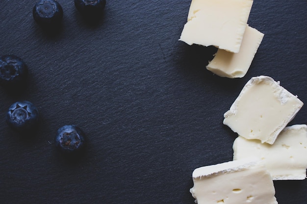 Brie cheese and blueberry on black cutting board. Camembert cheese slices with berries on black