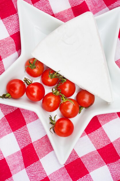 Brie cheese and cherry tomatoes on red tablecloth. close up