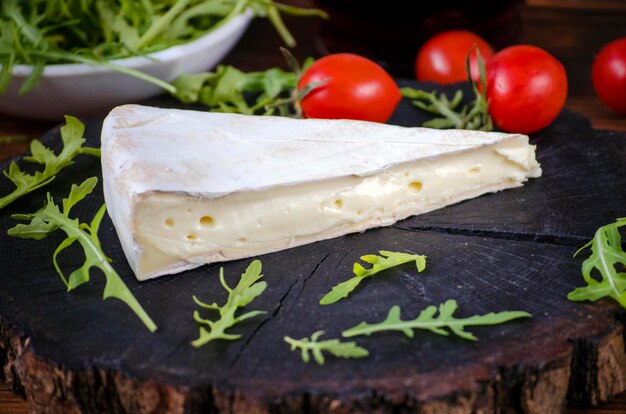 Brie cheese and lettuce leaves on dark wooden background