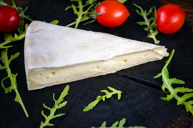 Brie cheese and lettuce leaves on dark wooden background