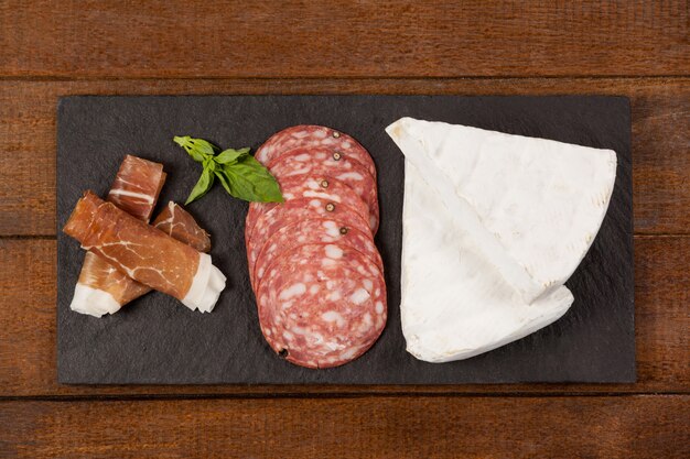 Brie cheese, salami, basil and sliced meat on black serving board