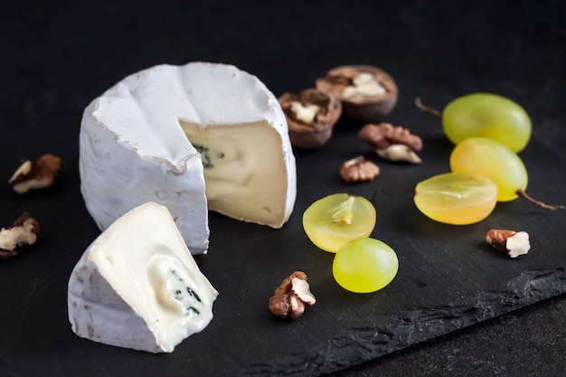 Brie soort kaas. Zachte kaas met druiven en walnoten op zwarte achtergrond