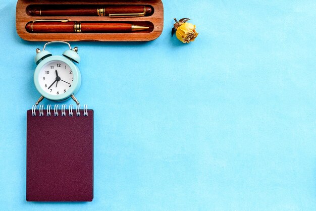 Briefpapierlay-out op een blauwe achtergrond, een notitieboekje op een lenteparker en een vintage wekker