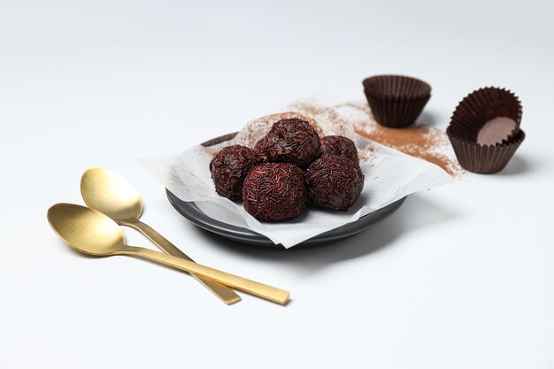 Brigadeiro on plate and golden spoons on white background