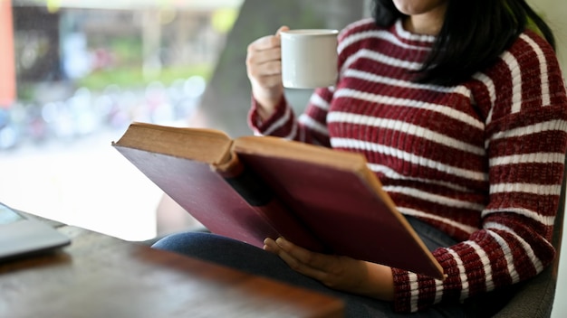 Bright Asian female college student concentrating on reading a book or textbook