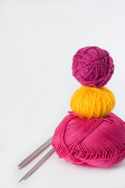 Bright balls of yarn and knitting needles lying on a white background