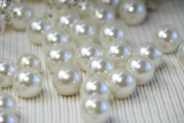 Bright beautiful white pearl beads scattered on white knitted\
textured background close up