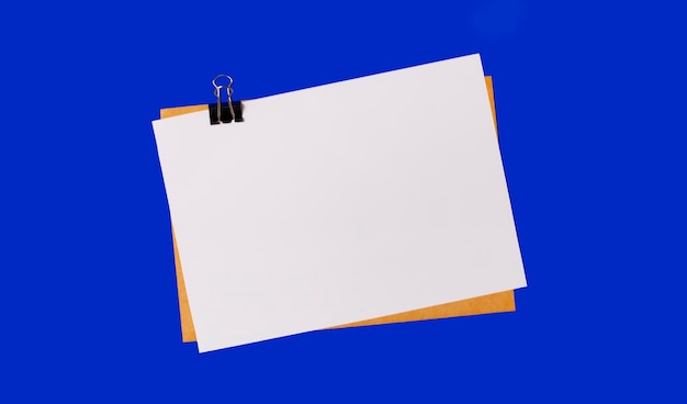 Photo on a bright blue background a craft envelope and a piece of paper with a place to insert text under a black paper clip copy space