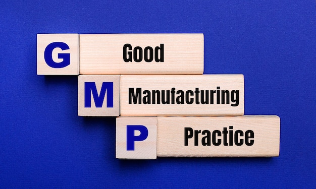 밝은 파란색 배경에 GMP Good Manufacturing Practice라는 텍스트가 있는 밝은 나무 블록 및 큐브