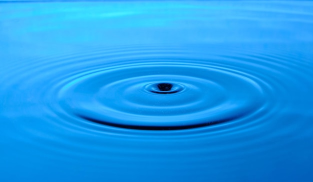 明るい青色の背景に地表水に落ちた滴から発散する円
