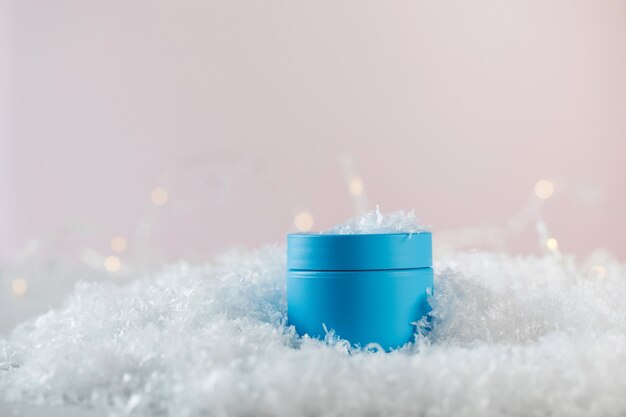 Bright blue blank jar of winter protective cosmetic product in artificial snow