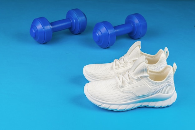 Bright blue dumbbells and white sneakers on a blue background.