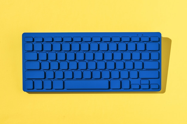 Photo bright blue keyboard in bright hard light on yellow background. monochrome image of office accessories.