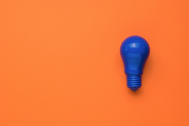 A bright blue light bulb on an orange background. Minimalism. Flat lay.