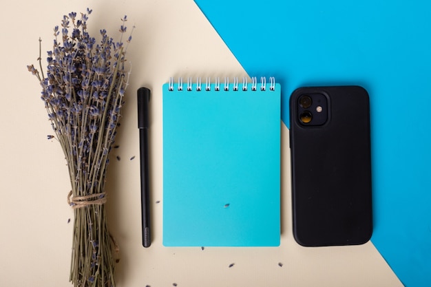 Bright blue notebook black pen smartphone and lavender beautifully lie on a beige background top vie...