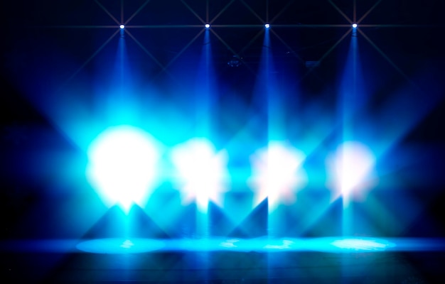 Bright blue rays of light from stage spotlights on a dark background