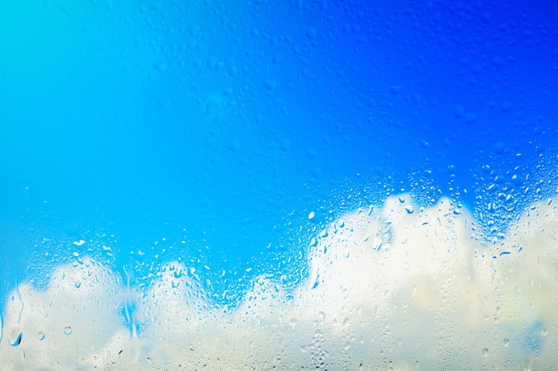 Bright blue sky with white clouds behind rain drenched glass.