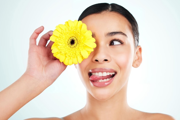 Яркий и игривый. Студийный снимок привлекательной молодой женщины, позирующей с желтым цветком на светлом фоне.