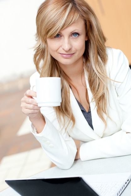 Bright businesswoman holding a cup of coffee in front of her laptop