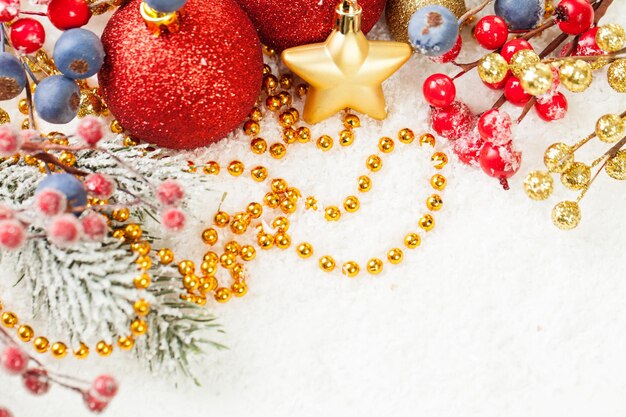 Bright Christmas composition with red baubles holly berries Xmas tree branch and golden garland on white snow background with empty copy space