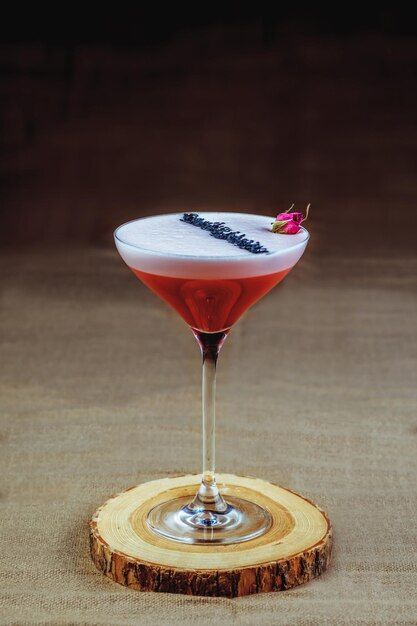 A bright cocktail with a small flower on a foam on a wooden stand. Cooling alcoholic beverage.