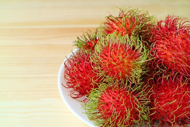 Bright Color Ripe Rambutan Fruits Piled on Plate on Wooden Table