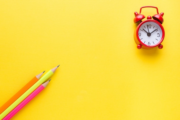 Bright colored pencils and alarm clock on yellow.