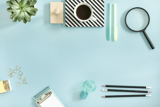 Bright and colorful composition of creative worspace with copy space and stylish offfice accessories as pencils, pens, notebooks and cup of coffee. Template. Blue background.