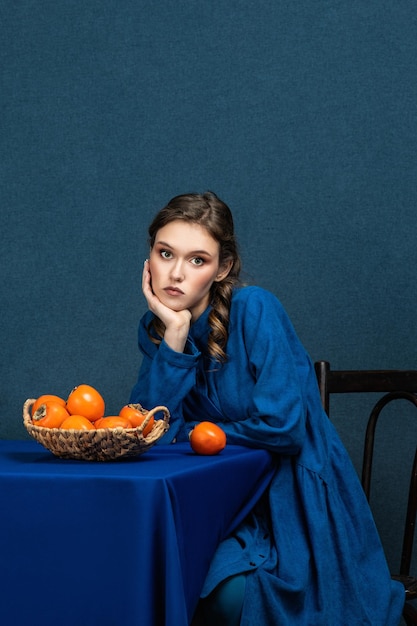 Bright combination a beautiful girl in a blue dress holds an orange persimmon