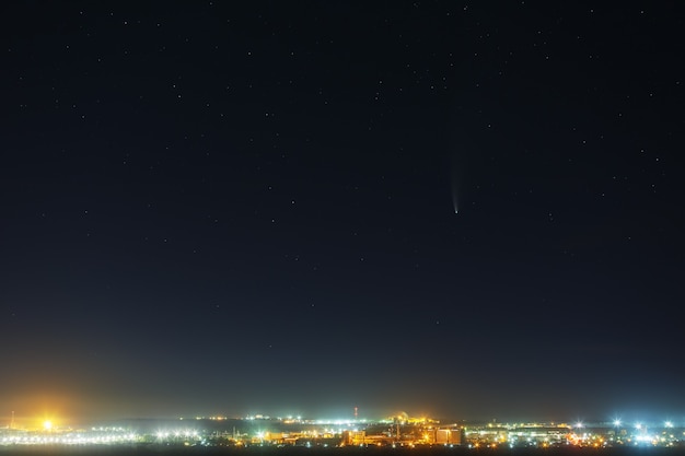 星空の明るい彗星C / 2020 F3（NEOWISE）。明るい街灯のある街の上の深宇宙オブジェクト。