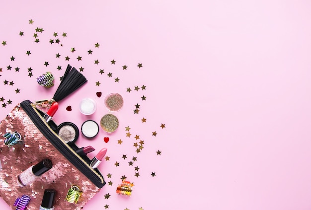 Bright composition of fashion accessories. Glitter sequins cosmetic bag with lipsticks, nail polishes and other objects. Object on soft pastel background with decorative tinsel. Flat lay, top view.