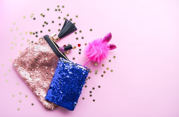 Bright composition of fashion accessories. Glitter sequins purse, notepad, funny pen and decorative tinsel. Different objects on soft pastel background. Flat lay, top view.