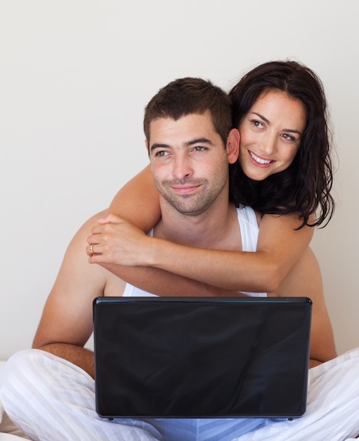 Bright couple using a laptop sitting on a bed